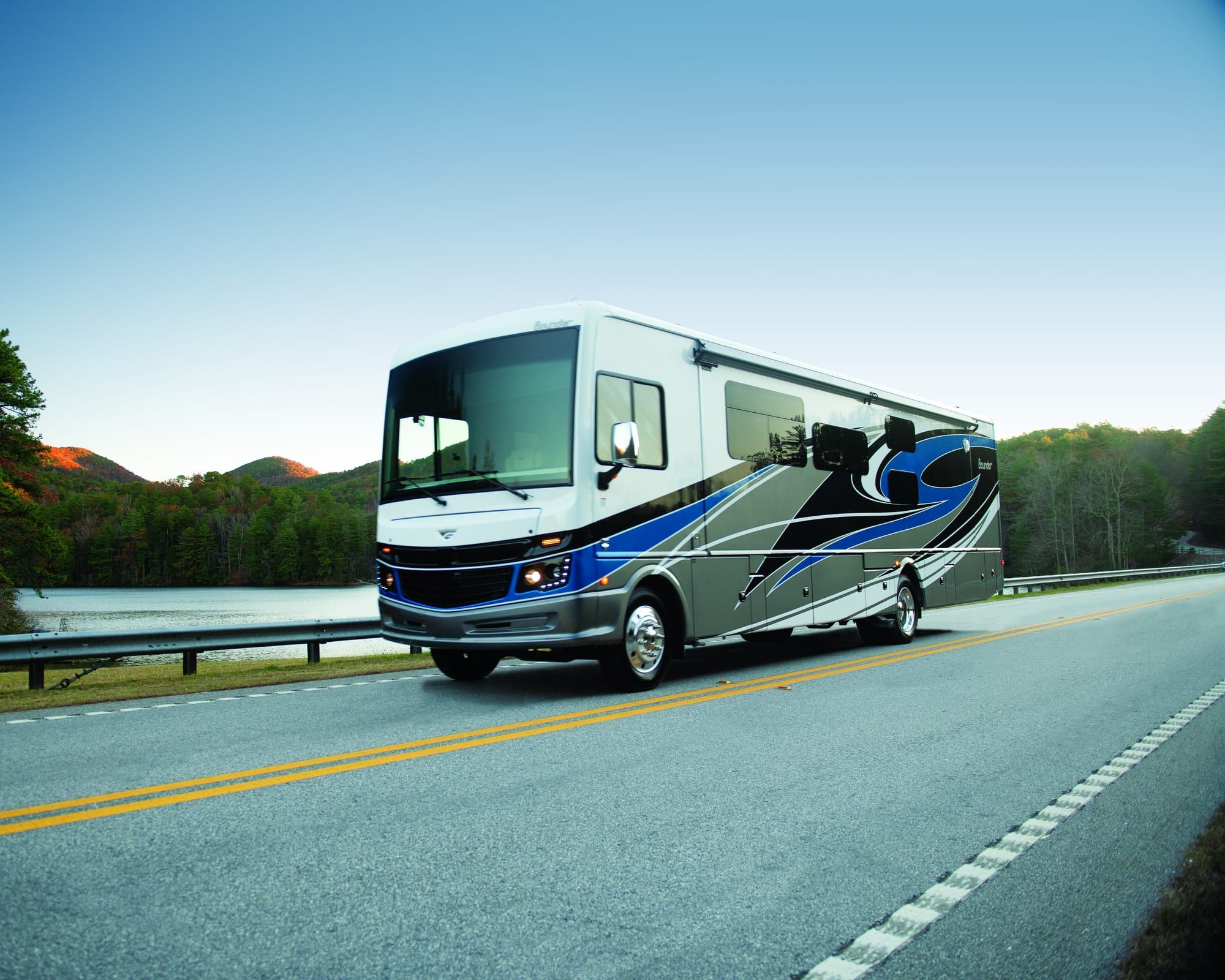 A Fleetwood Bounder Class A motorhome on a two-lane road beside a lake at dusk.