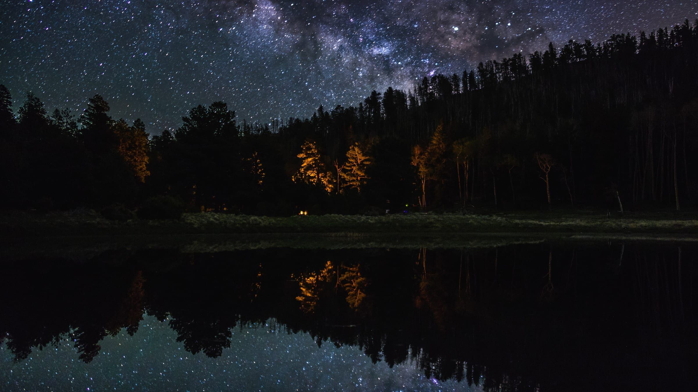 The Milky Way over a dark pine forest, reflected in a still pond at Lockett Meadow campground in Arizona.